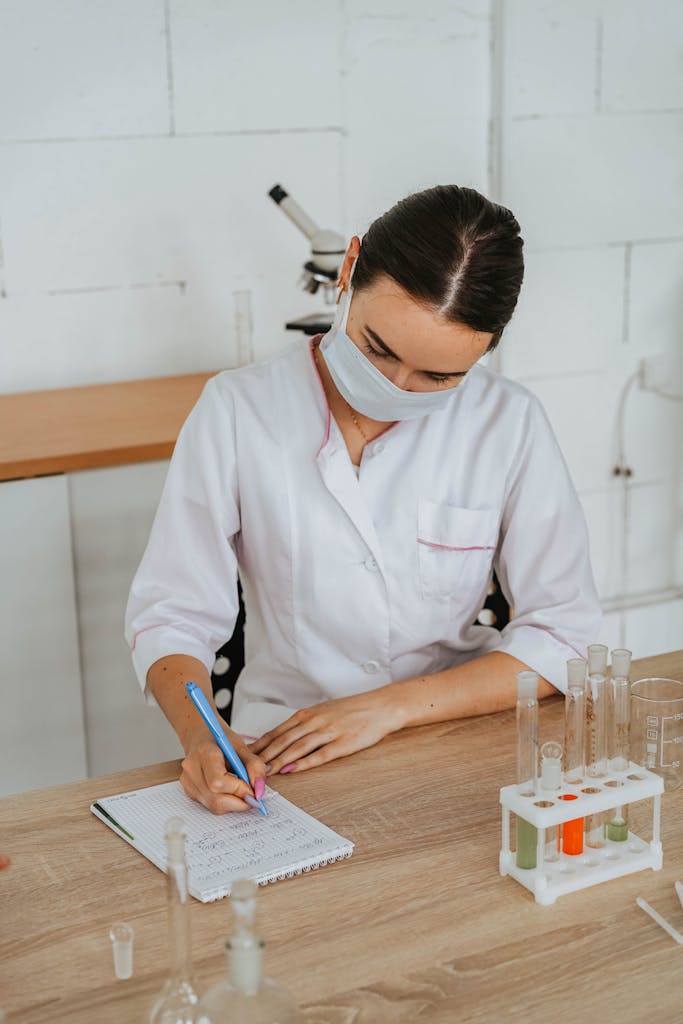 A female scientist in a lab coat writing notes, surrounded by test tubes and a microscope.